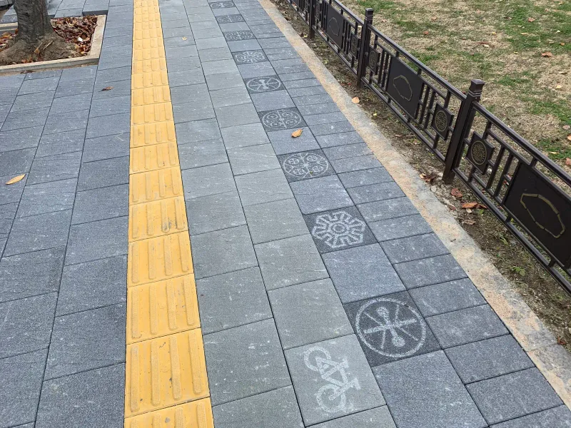 풍납토성 보도. 회색 사암 느낌 블록 보도에 노란 점자블록이 곧게 이어지고, 전통 문양 난간 쪽으로 문양이 새겨진 블록이 한 줄로 박혀 있다.