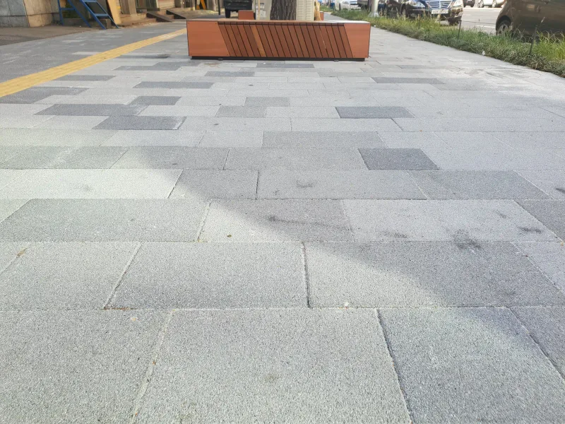 중구 동호로 도심 보도. 밝은 회색과 짙은 회색 대형 블록이 크기를 섞어 어긋나게 깔려 있고 노란 점자블록과 목재 화분 벤치가 보인다.