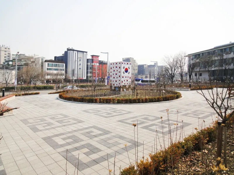 보훈공단 수원보훈원 원형 화단 광장. 밝은 회색 블록 바탕에 짙은 회색 블록으로 전통 번개무늬를 넣은 바닥이 화단 둘레로 펼쳐진다.