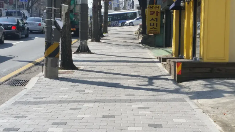 소방안전본부 일대 상가 앞 보도. 전신주와 가로수 옆으로 회색 블록이 넓게 깔리고 짙은 회색 블록 띠가 가로로 놓여 있다.