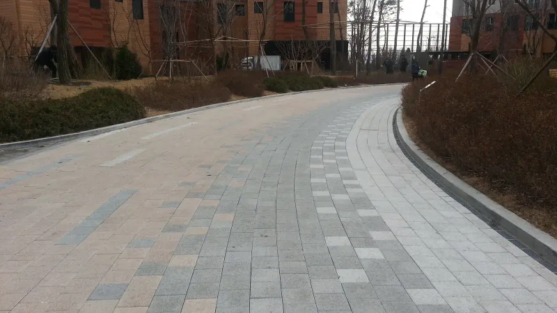 영통 래미안 마크원 단지 내 곡선 차로. 회색 블록 사이로 밝은 블록 띠가 휘어진 길을 따라 이어지고, 화단 너머 주황빛 외벽의 아파트가 보인다.