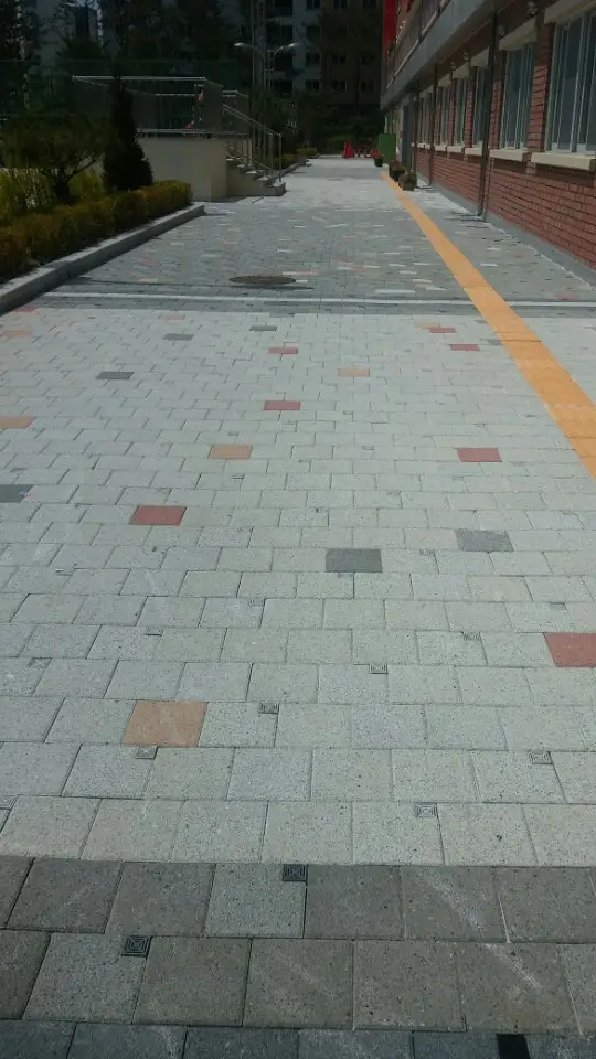 위례 한빛초등학교 벽돌 교사동을 따라 난 보행로. 회색 블록 포장에 색 블록이 드문드문 섞여 있고 한쪽으로 노란 점자블록 선이 지난다.