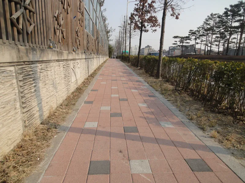 수원 세류동 보도를 반대 방향에서 본 모습. 적색 블록 보도 왼쪽으로 문양이 새겨진 옹벽과 방음벽이 길게 이어진다.