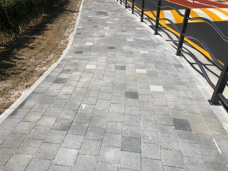 해운대 청사포 입구 교차로 보도. 짙은 회색·연회색 블록이 섞여 깔린 보도가 검은 난간을 따라 완만하게 휘어지며 이어진다.