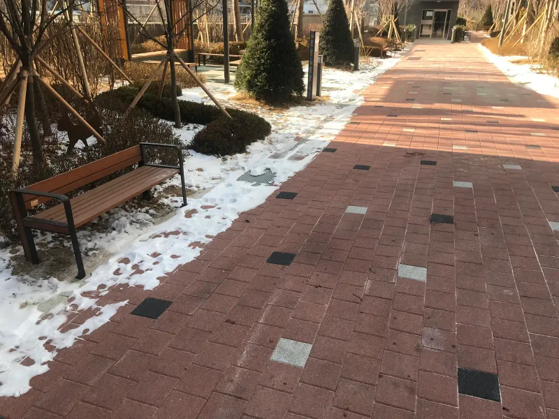 북한산 더샵 쉼터 갈림길. 적갈색 블록 길이 T자로 갈라지고 눈 덮인 화단 옆에 나무 벤치가 놓여 있다.