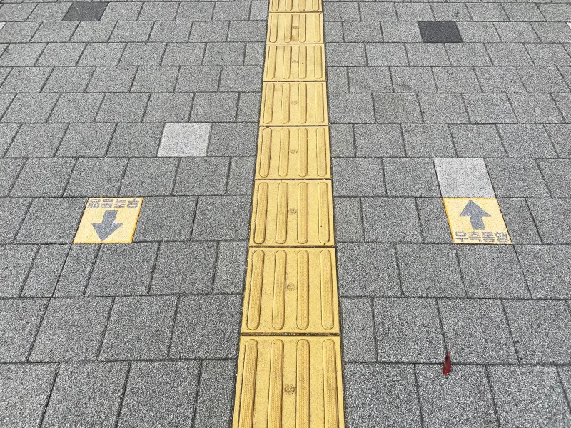 마포구 관내 보도정비 구간 바닥 근접. 회색 블록 위로 노란 점자블록이 지나고, 양옆에 '우측통행' 화살표가 새겨진 노란 싸인블록이 서로 반대 방향으로 놓여 있다.