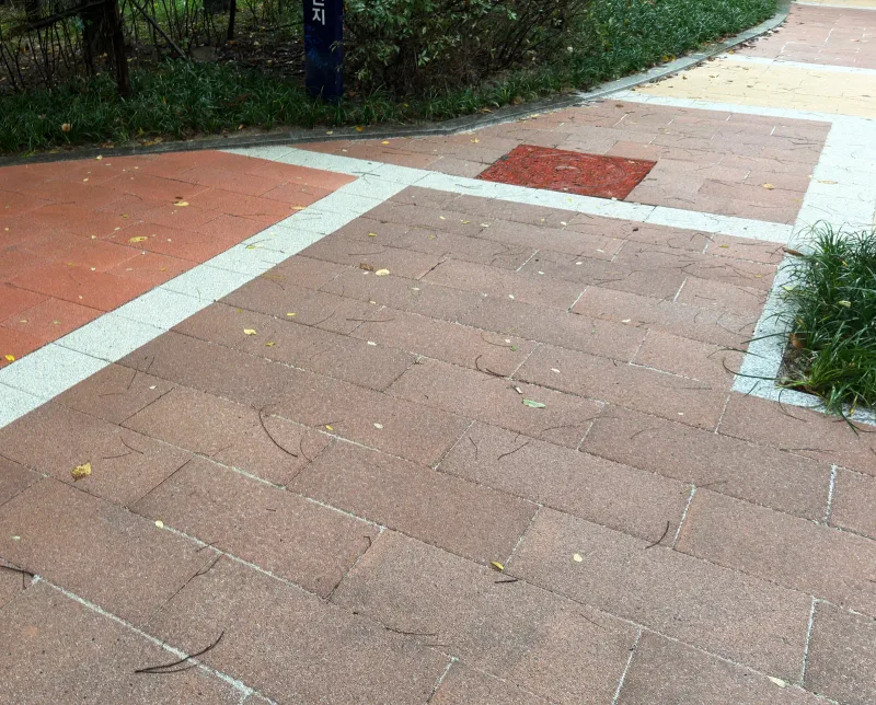 상암동 매봉산로 포장 근접 사진. 적갈색 판형 블록 면과 밝은 회색 띠가 만나는 부분에 붉은 정사각형 덮개가 끼워져 있다.