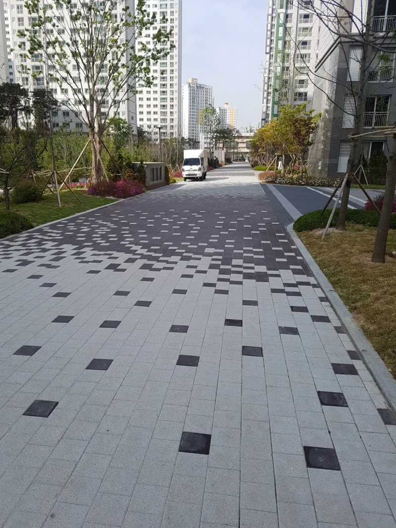 시흥 배곧 한신휴플러스 동 앞 진입로. 밝은 회색 블록 위에 짙은 회색 블록이 점점 많아지며 안쪽으로 짙어지는 무늬를 이룬다.