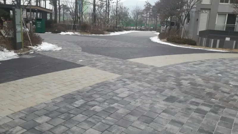 에일린의 뜰 단지 내 갈림길. 여러 색이 섞인 회색 계열 블록 도로와 베이지색 블록 띠가 만나고 뒤로 아파트 동이 보인다.