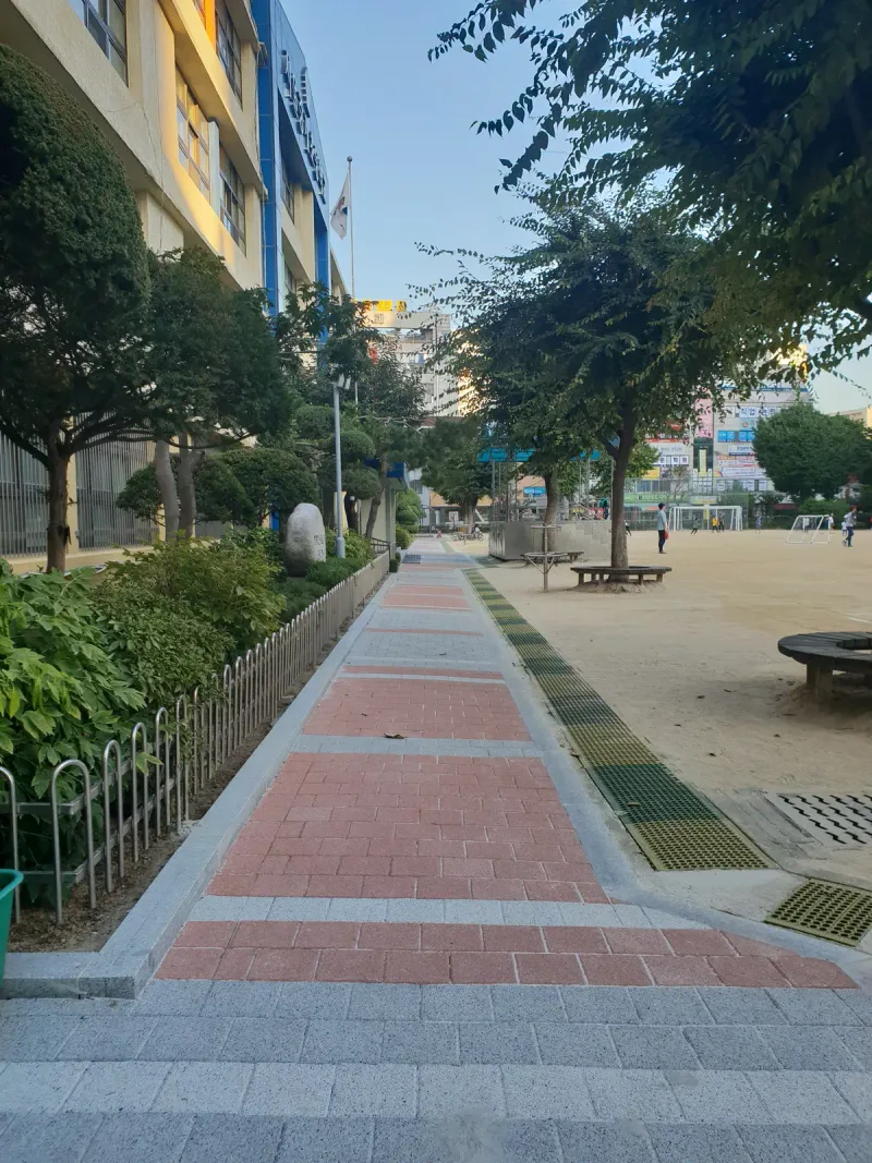 중계초등학교 울타리 옆 통로를 세로로 본 모습. 회색 블록 길에 적갈색 블록 띠가 일정한 간격으로 가로질러 깔려 있다.