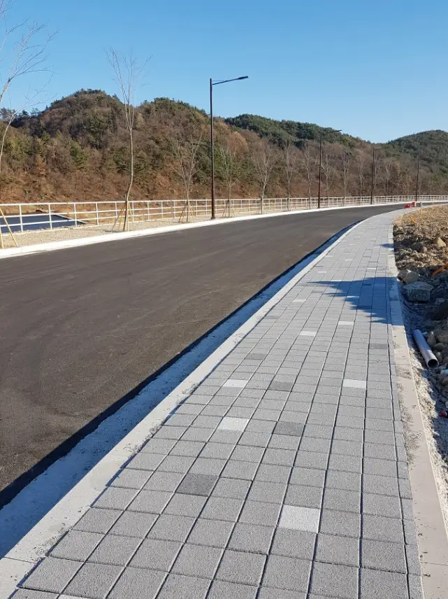 울주 온양 신설 도로변 보도. 회색 사각 블록에 밝은 회색·짙은 회색 블록이 드문드문 섞인 보도가 차도를 따라 곡선으로 이어지고 뒤로 산이 보인다.