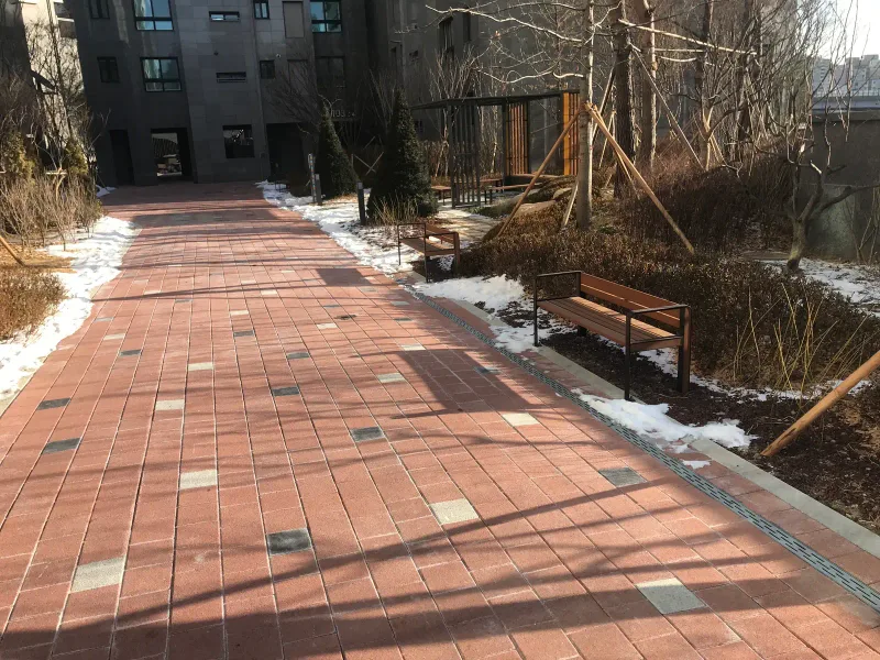 북한산 더샵 동 사이 산책로. 적갈색 블록 길에 흰색·검은색 블록이 드문드문 박혀 있고 옆으로 나무 벤치가 줄지어 있다.