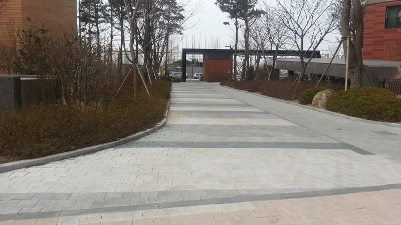 영통 래미안 마크원 단지 안 보행로. 밝은 회색 블록 길에 짙은 회색 블록 가로 띠가 일정 간격으로 들어가 있고, 끝에 단지 문주와 소나무가 보인다.