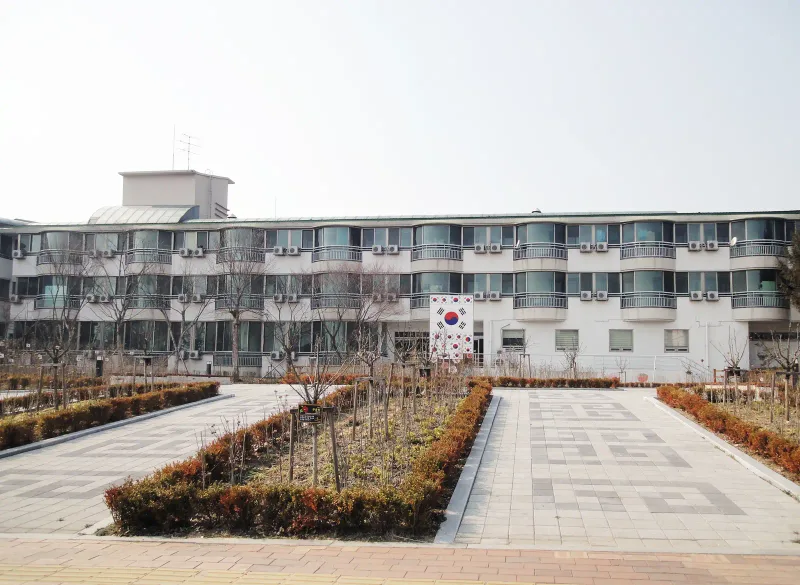 수원보훈원 건물 앞 정원. 밝은 회색 블록 보행로가 관목 화단 사이로 건물 입구까지 곧게 이어지고 바닥에 짙은 무늬가 들어가 있다.