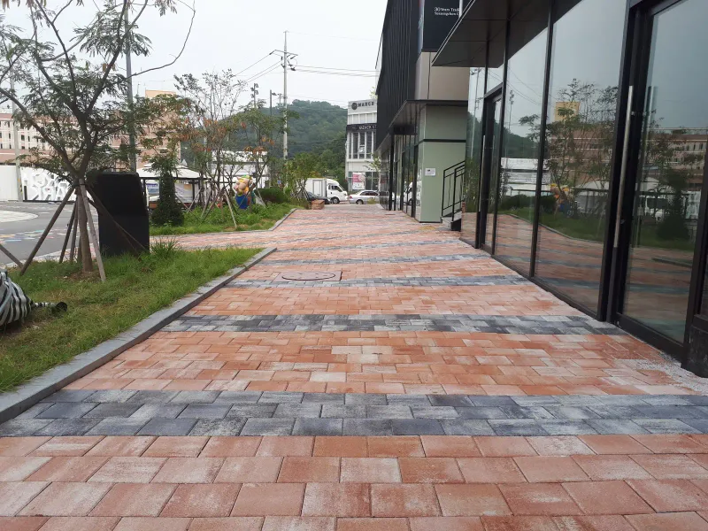 마치에비뉴 2차 유리 상가 전면 보도. 분홍빛 블록 길에 짙은 회색 가로 띠가 반복되고 옆에 잔디와 가로수가 있다.