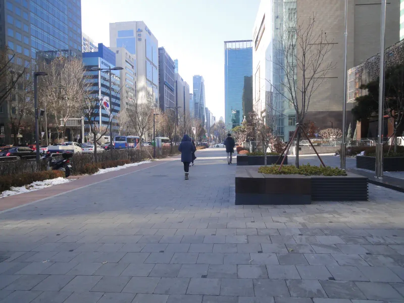 영동대로 삼성동 보도와 건물 앞 공간. 회색 대형 블록 바닥 위에 낮은 사각 화단이 놓여 있고 멀리 고층 빌딩가를 따라 보행로가 이어진다.
