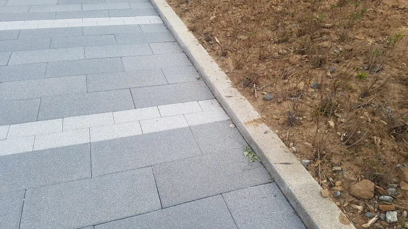유스트림 광장 경계부 근접. 회색 블록과 밝은 회색 블록 띠가 화강석 경계석과 흙 화단에 맞닿아 있다.