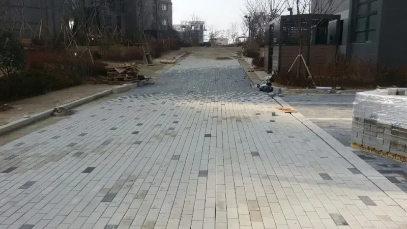 전주 우미린 단지 진입 보행로 시공 중 모습. 밝은 회색 블록에 짙은 블록이 드문드문 섞인 길이 깔려 있고 오른쪽에 블록 더미가 쌓여 있다.
