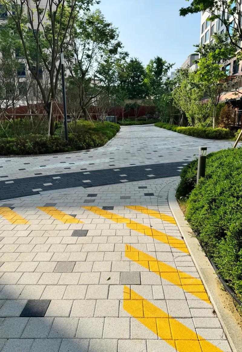 e편한세상 구성역 플랫폼시티 경사 보행로 세로 사진. 밝은 회색 블록 위에 노란 빗금 노면 표시가 있고 길이 화단 사이로 굽어 간다.