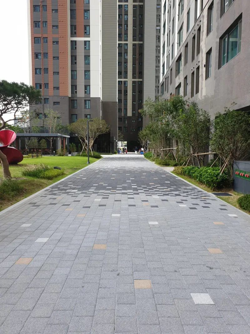 e편한세상 부산항 동 사이 산책로. 회색 블록 길에 짙은 회색·흰색 블록이 흩어져 있고 양옆에 잔디와 조경수가 있다.
