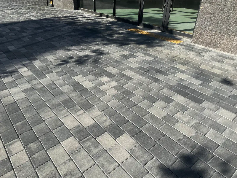 한화 포레나 당산 보도 블록 근접. 흰색·회색·짙은 회색 직사각형 블록이 불규칙하게 섞여 있고 나뭇잎 그림자가 얼룩지게 드리운다.