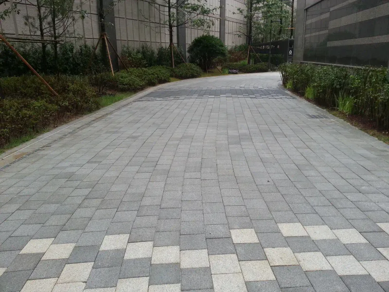 아현동 현장 단지 내 경사 통로. 회색 블록이 넓게 깔린 길 앞쪽에 밝은 블록이 가로 띠를 이루고, 양옆으로 화단과 건물 벽이 있다.