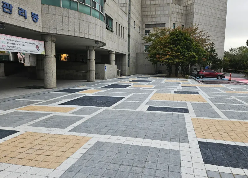 을숙도 들락날락 광장 건물 앞. 회색·짙은 회색·베이지색 블록 구획이 흰 띠와 함께 건물 기둥 아래까지 이어진다.