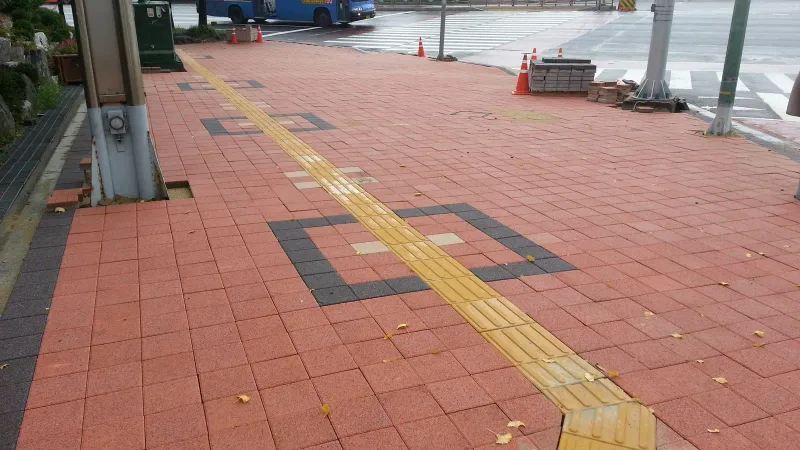 인천 연수구 교차로 앞 보도. 적갈색 블록 바닥에 짙은 회색 블록으로 네모 테두리 무늬를 넣었고 노란 점자블록이 사선으로 꺾여 횡단보도 쪽으로 이어진다.