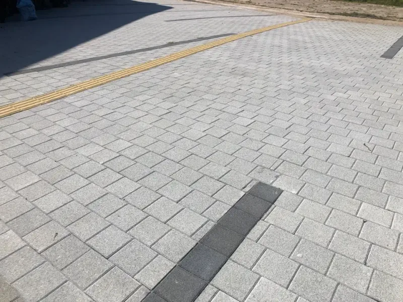 기장군 수산물체험장 넓은 보도. 밝은 회색 블록 바탕에 짙은 회색 블록 띠가 가로지르고 노란 점자블록 선이 지난다.