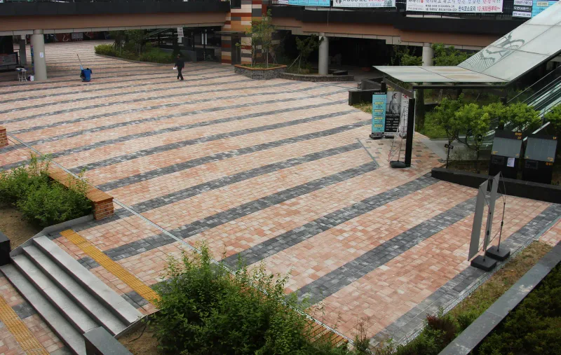 마치에비뉴 2차 광장과 계단 진입부. 연분홍·살구색 블록 사이로 짙은 회색 줄무늬가 길게 뻗고 계단 옆으로 노란 점자블록이 이어진다.