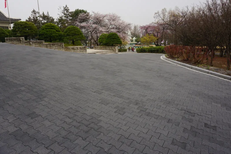 국립서울현충원 청사 진입 차로. 짙은 회색 맞물림 차도블록이 완만하게 휘어지는 넓은 길에 깔려 있고 멀리 벚꽃과 조경수가 보인다.