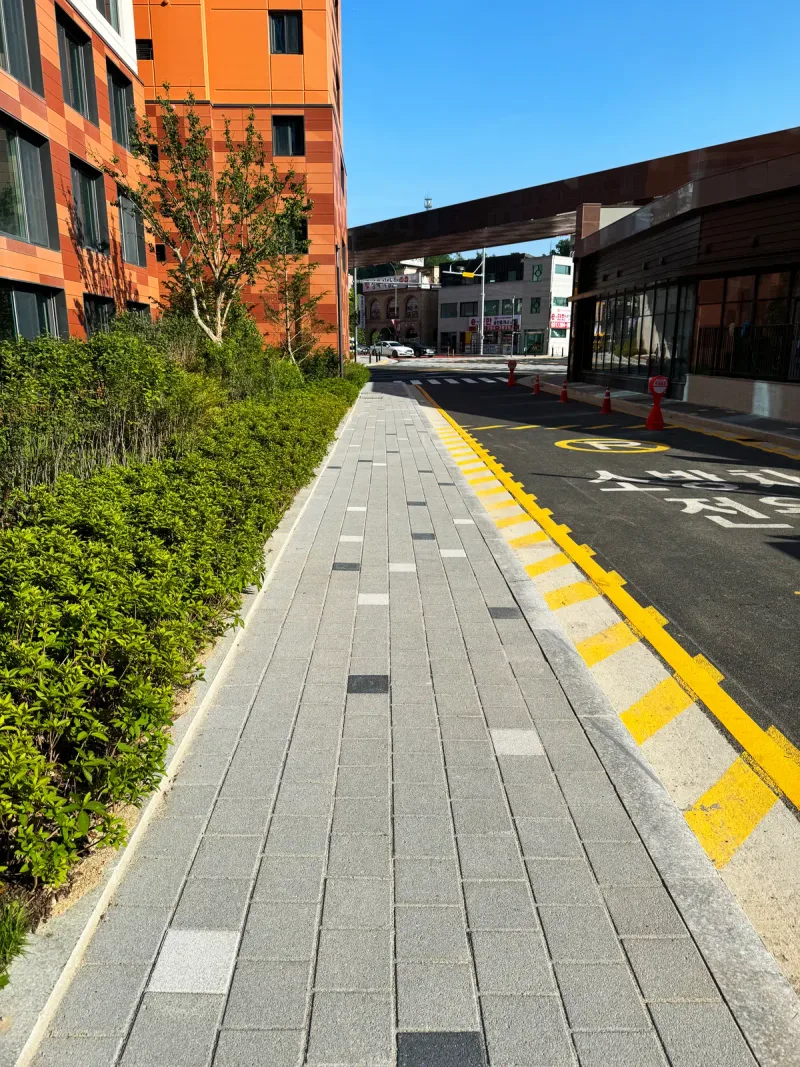 e편한세상 구성역 플랫폼시티 단지 바깥 보도(세로 사진). 회색 블록 보도에 흰색·짙은 회색 블록이 점점이 섞여 있고 옆으로 차도가 지난다.