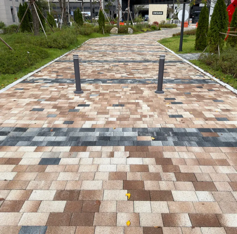 동탄2 숨마데시앙 보행로(세로 사진). 베이지·갈색 혼합 블록 길에 짙은 회색 띠가 가로로 놓이고 입구에 볼라드 두 개가 서 있다.