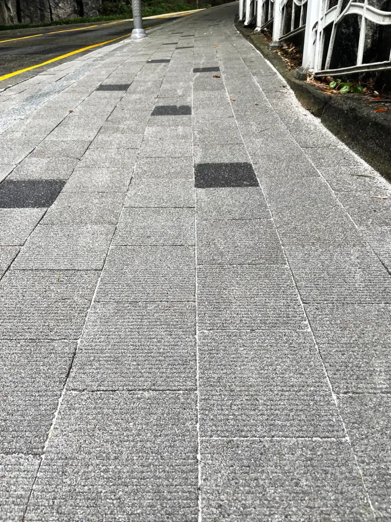 중구 보도유지공사 구간 내리막 곡선 보도. 줄무늬가 새겨진 회색 직사각형 블록 사이에 검은 블록이 흩어져 박혀 길을 따라 이어진다.