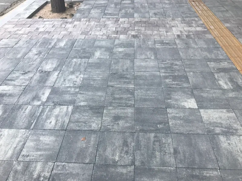 잠실관광특구 가로수 옆 보도 근접. 크기가 다른 직사각형 블록이 회색·흰색 얼룩 무늬로 섞여 깔려 있고 오른쪽에 노란 점자블록이 있다.