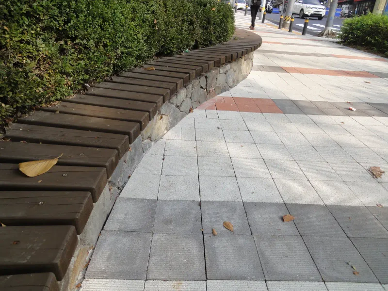 숭실대학교 중문 앞 곡선 좌석 디테일. 돌 쌓기 위에 나무 널을 얹은 곡선 좌석이 연회색 블록 보도와 맞닿고 적갈색 줄이 뒤로 이어진다.