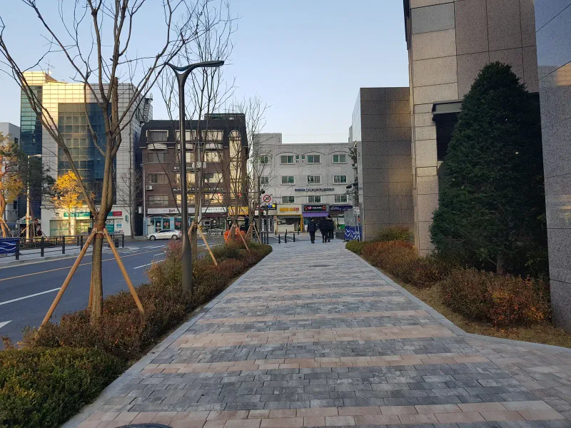 일원동 래미안 루체하임 단지 출입 보행로. 분홍·회색 톤이 섞인 블록 길이 관목 화단 사이로 뻗어 바깥 도로와 이어진다.