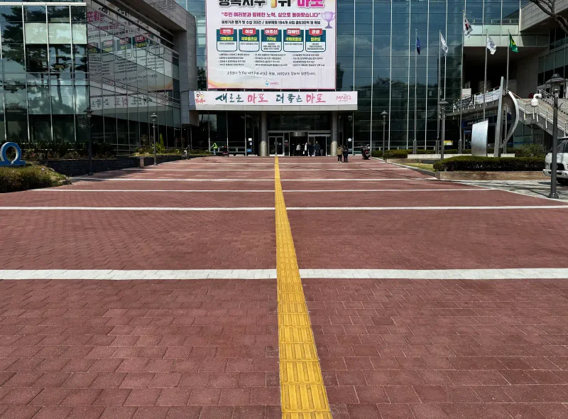 마포구청 앞 광장. 붉은 블록 바닥을 흰 띠가 가로로 나누고 가운데로 노란 점자블록이 청사 입구까지 곧게 이어진다.