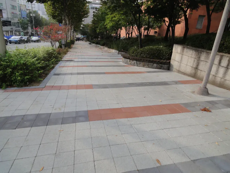 숭실대학교 중문 옆 옹벽 앞 보도. 넓은 연회색 블록 길에 적갈색·짙은 회색 블록 띠가 가로로 깔리고 한쪽에 콘크리트 옹벽과 가로수가 있다.