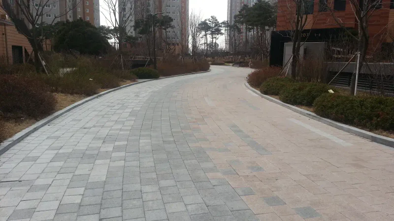 영통 래미안 마크원 단지 내 곡선 도로를 다른 방향에서 본 모습. 회색·베이지 블록이 섞여 깔린 길이 관목 화단 사이로 부드럽게 굽어 이어진다.