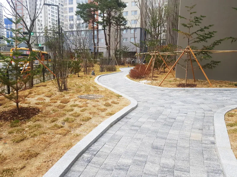 동탄2 아이파크 정원 산책로. 흰 경계석을 두른 회색 블록 길이 마른 잔디 사이로 S자로 굽어 나간다.