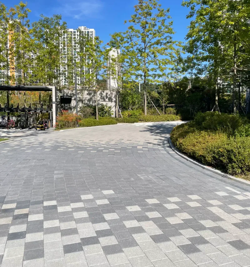 e편한세상 지축 센텀가든 자전거 보관소 앞 굽은 길. 회색 사각 블록 사이에 짙은 블록이 체크 무늬로 섞여 있고 둥근 관목 화단이 곡선을 이룬다.