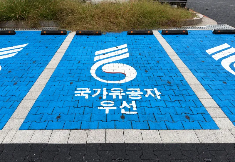 잠실한강공원 국가유공자 우선 주차 칸. 파랗게 칠한 차도 블록 위에 흰 표장과 글씨가 그려져 있고 앞쪽에 멈춤턱이 줄지어 있다.
