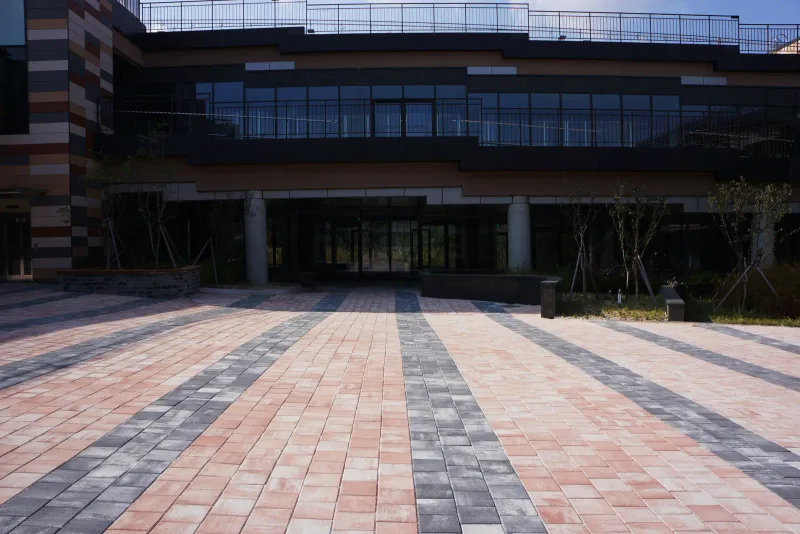 마치에비뉴 2차 상가 건물 정면 쪽 광장. 분홍빛 블록 바탕에 짙은 회색 띠가 건물 쪽으로 모이며 원근감 있는 줄무늬를 만든다.