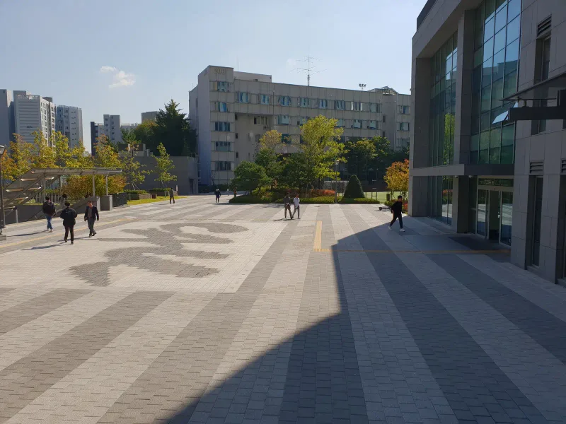 중앙대학교 건물 앞 광장. 회색 줄무늬 블록 바닥 가운데에 짙은 회색 블록으로 큰 곡선 무늬를 그려 넣었고 뒤로 강의동이 서 있다.