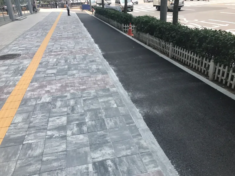 잠실관광특구 보도와 자전거도로. 노란 점자블록이 지나는 회색 계열 블록 보도 오른쪽으로 검은 자전거도로와 흰 울타리 화단이 이어진다.