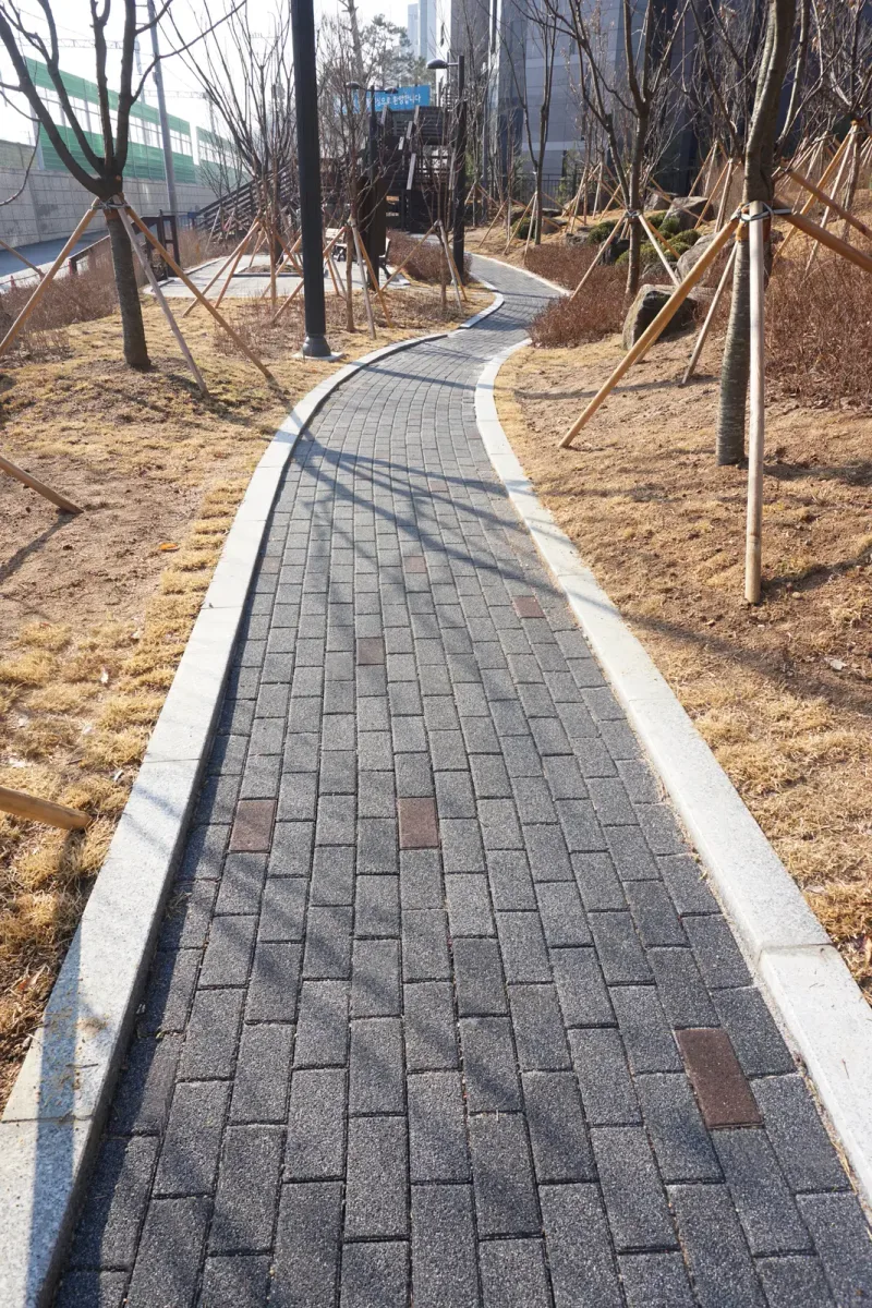 월계 두산위브 단지 녹지 사이 오솔길을 세로로 담은 모습. 밝은 경계석 사이 짙은 회색 블록 길에 적갈색 블록이 드문드문 섞여 있다.