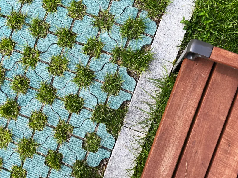 DMC 파인시티자이 잔디블록과 벤치 디테일. 연청록 잔디블록 틈마다 풀이 자라고 옆으로 경계석과 목재 벤치가 맞닿아 있다.