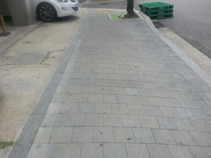 합정 배수분구 골목 보도. 짙은 회색 경계 블록 안쪽으로 회색 직사각형 블록이 엇갈려 깔렸고, 블록 모서리마다 작은 사각 덮개가 보인다.