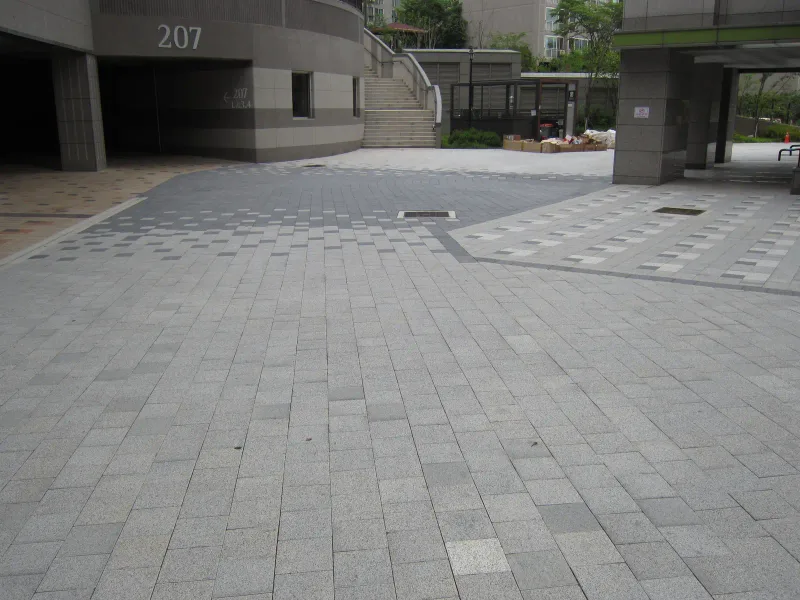 현대 엠코타운 207동 필로티 앞 마당. 회색 블록 바닥에 밝고 어두운 블록이 사각 테두리 무늬를 이루고 뒤로 계단이 보인다.